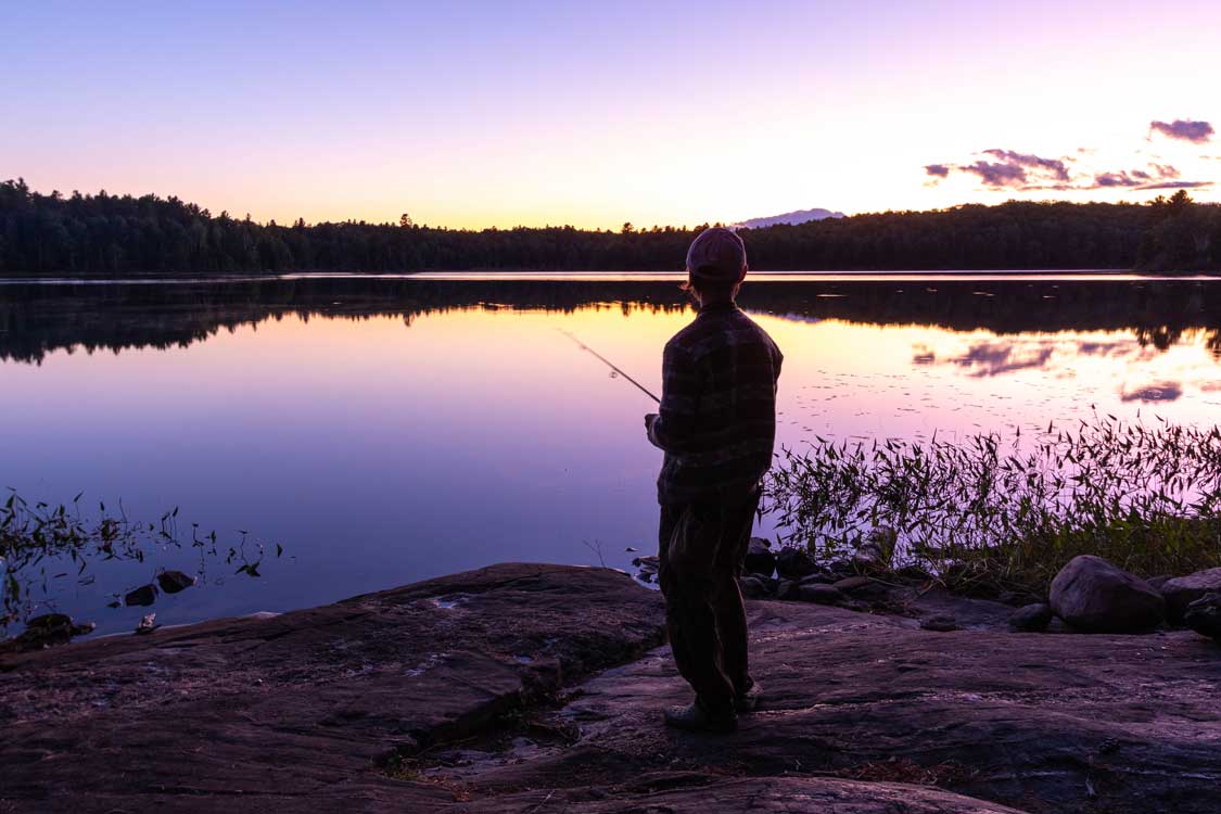 Fisherman casting on the shores of a lake under a pink sunset