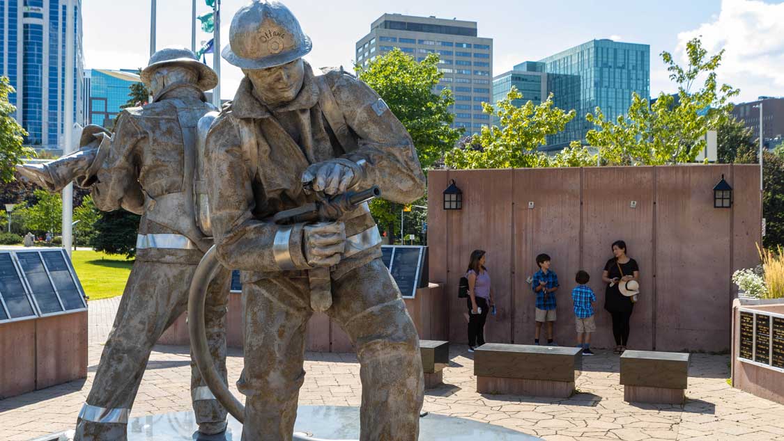 A woman talks to a mother and her children about a monument to firefighters on an Ottawa art tour