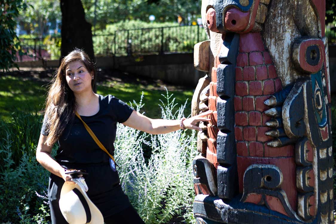 A metis woman holding a hat stands next to a Totem pole in Ottawa's Confederation Park