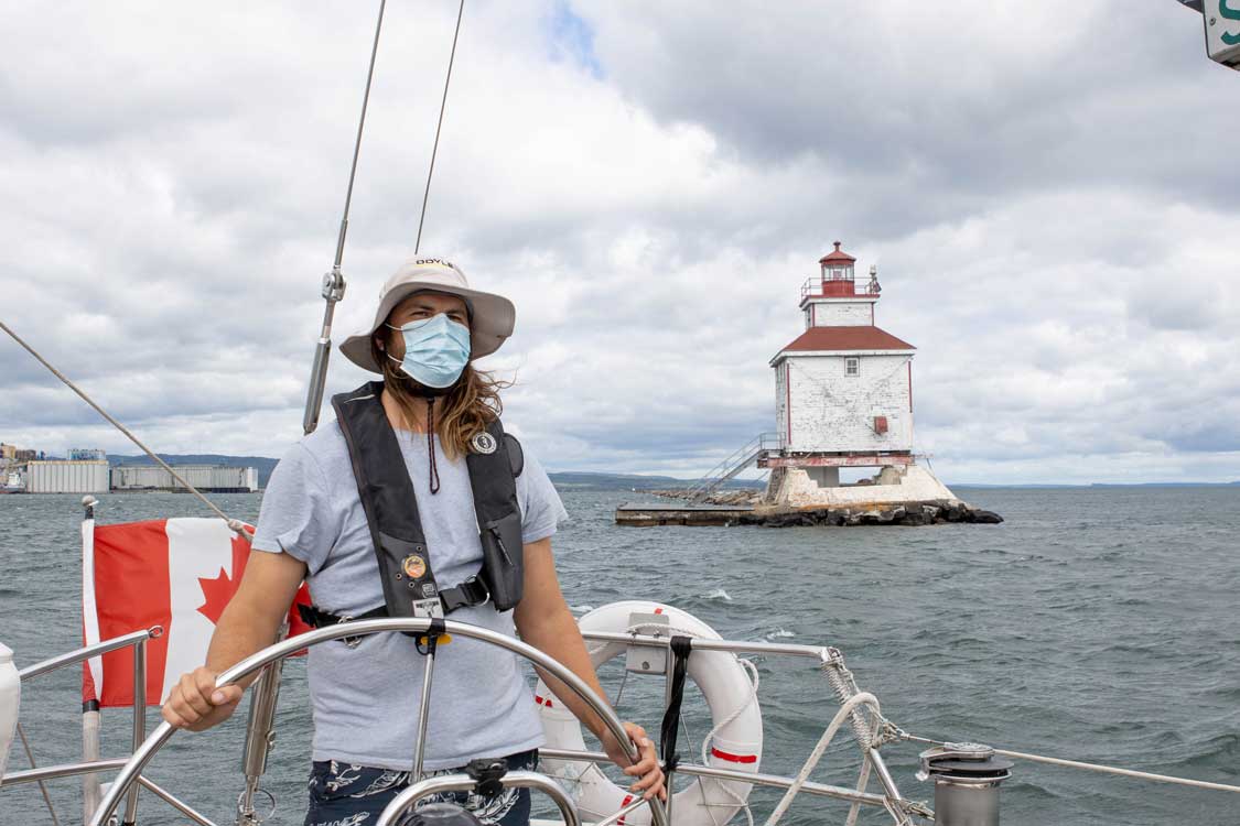 A boat captain passes a lighthouse on a boat with a Canadian flag flowing in the background