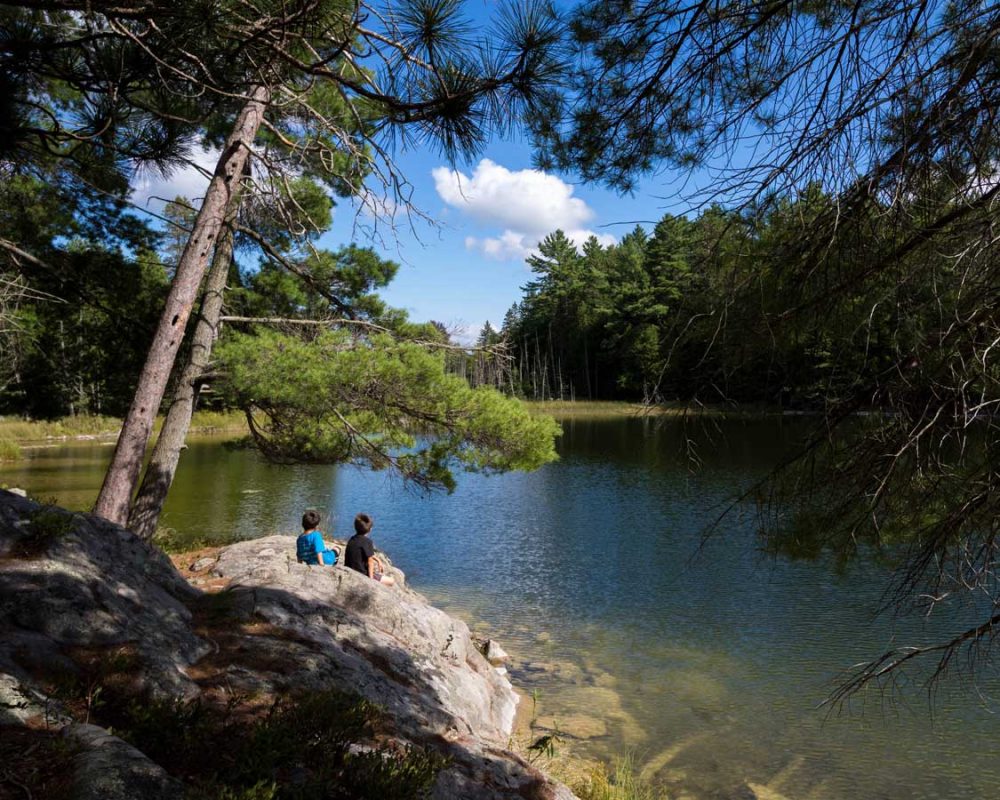 Two boys sitting on a rock next to a lake in Petroglyphs Provincial Park in Peterborough, Ontario