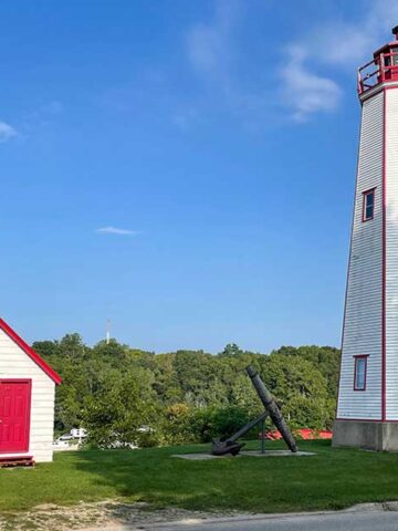 Things to do in Port Burwell Ontario - A white lighthouse with red trim against a green forest