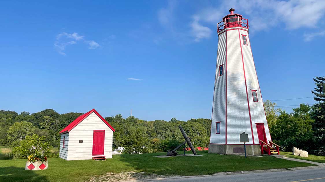 Things to do in Port Burwell Ontario - A white lighthouse with red trim against a green forest