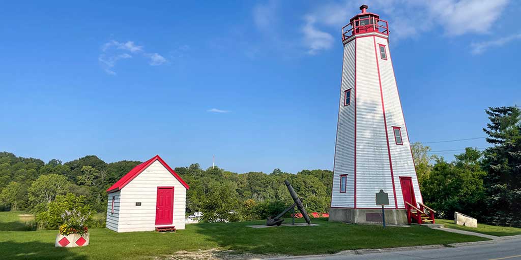 Things to do in Port Burwell Ontario - A white lighthouse with red trim against a green forest