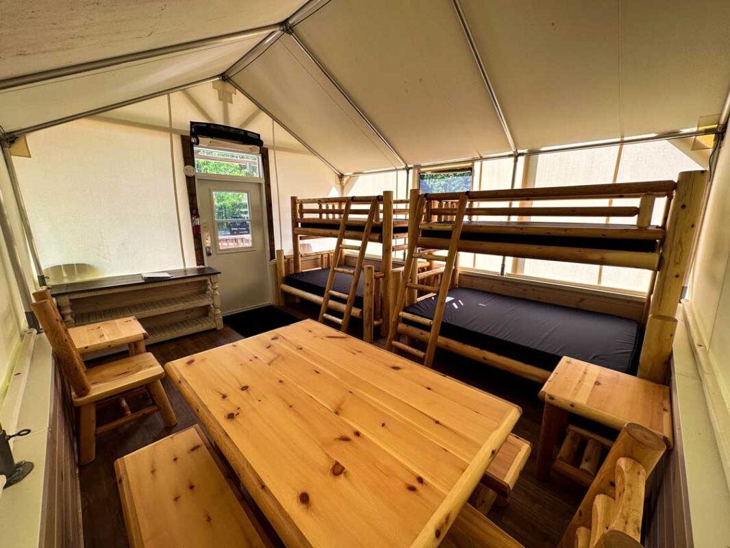 Two bunk beds and a kitchen table inside a soft-sided camping tent