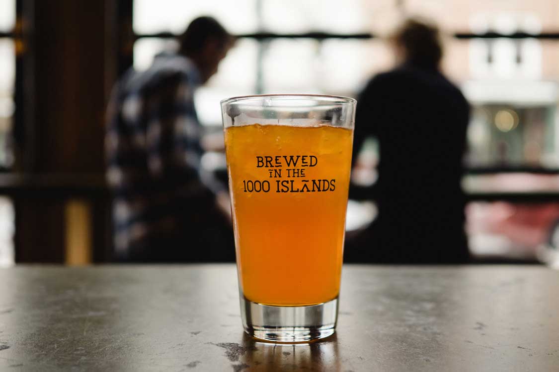 A beer on a bar in a glass that says 