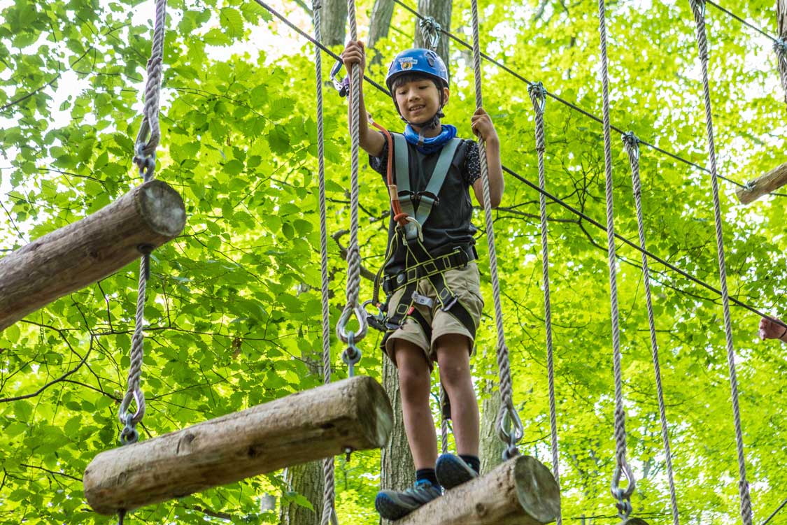 A boy with a blue helmet enjoying treetop trekking in Brockville, Ontario