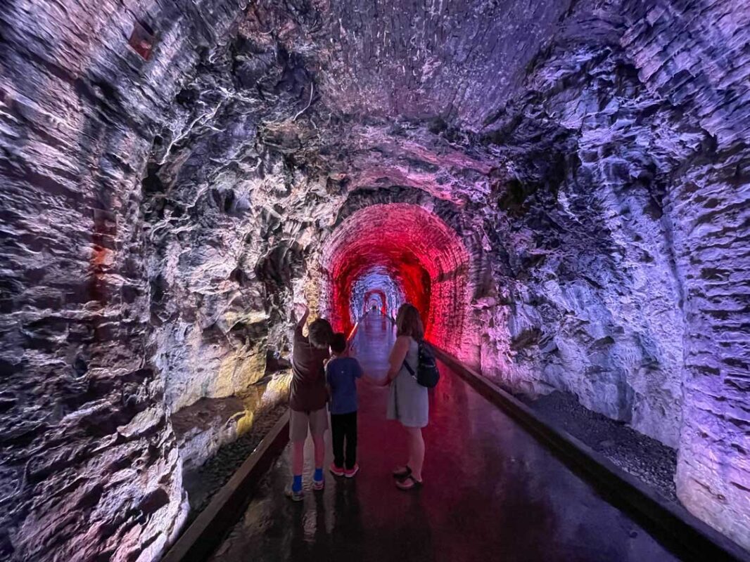 A family walks through a stone tunnel lit with colourful LED lights in the Brockville Railway Tunnel