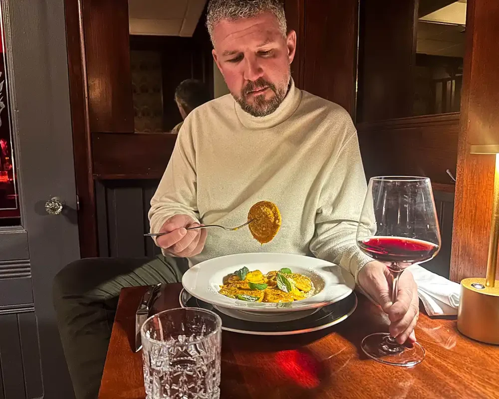 A man in a white turtleneck sweater dining on raviolo at Churchill's North Bay