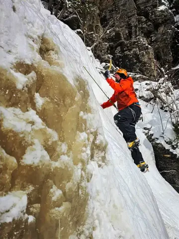 A man prepares to dig an ice axe into a frozen waterfall while ice climbing in Thunder Bay, Ontario
