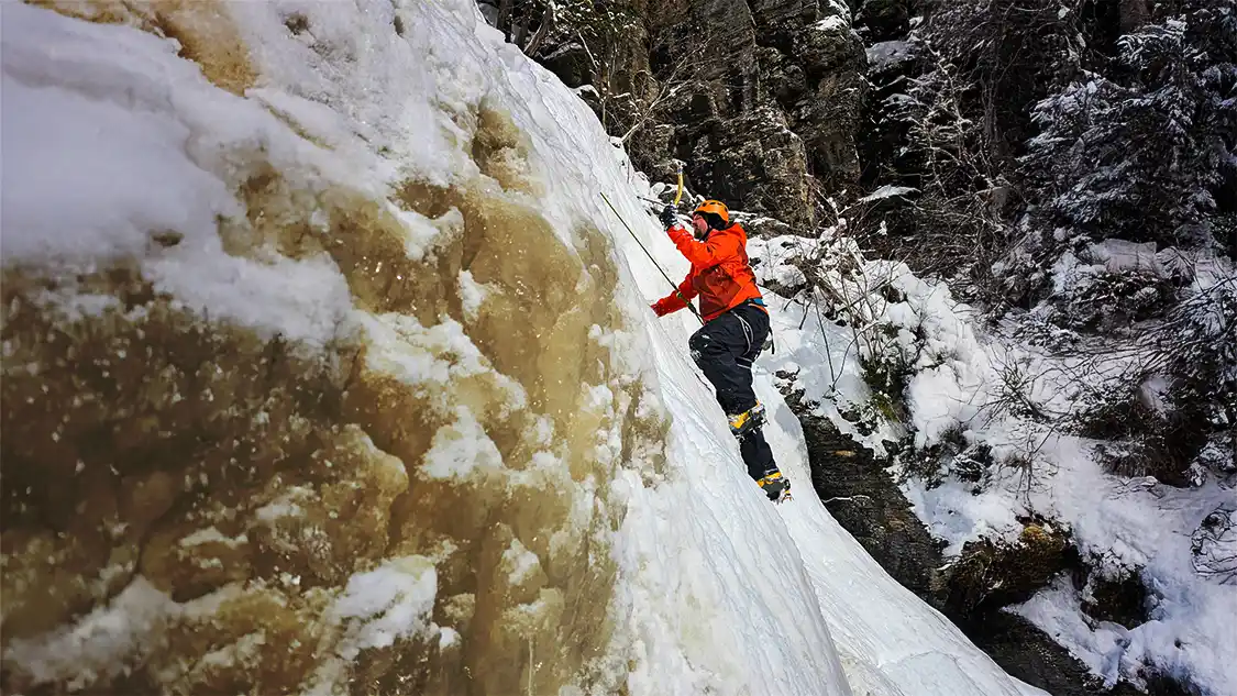 A man prepares to dig an ice axe into a frozen waterfall while ice climbing in Thunder Bay, Ontario